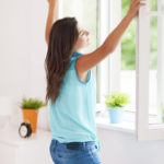 Young woman opening window in living room